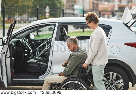 Side View Portrait Of Mature Couple With Man In Wheelchair By Car In Parking Lot Outdoors, Copy Spac