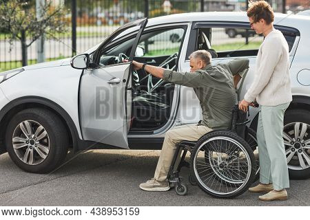 Portrait Of Woman Helping Man In Wheelchair Enter Car In Parking Lot Outdoors, Copy Space