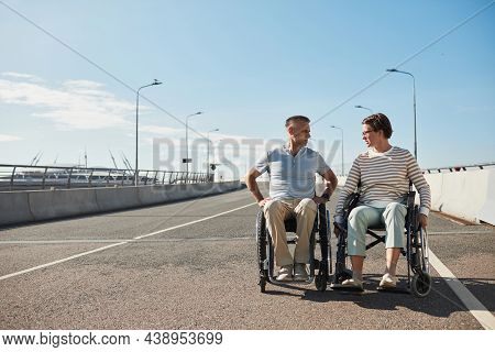Full Length Front View Portrait Of Adult Couple In Wheelchairs Chatting Outdoors And Enjoying City L