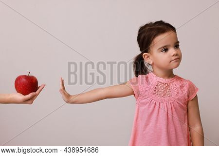 Cute Little Girl Refusing To Eat Apple On Grey Background
