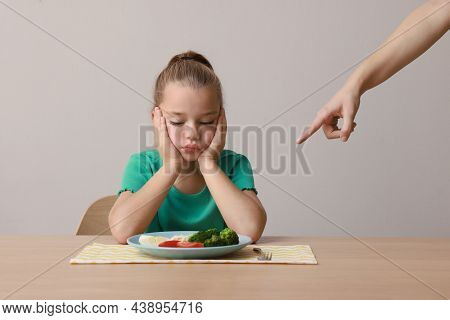 Cute Little Girl Refusing To Eat Her Breakfast At Table On Grey Background
