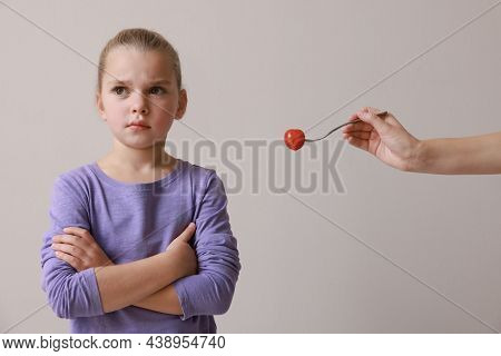 Cute Little Girl Refusing To Eat Tomato On Grey Background