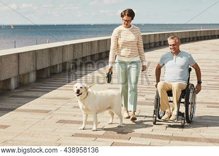 Portrait Of Adult Couple With Man In Wheelchair Walking Dog Outdoors By River, Copy Space