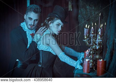 Handsome bloodthirsty male vampire going to bite an innocent beautiful woman in his arms. Dark vintage castle background. Halloween. Vampires of the 19th century. 