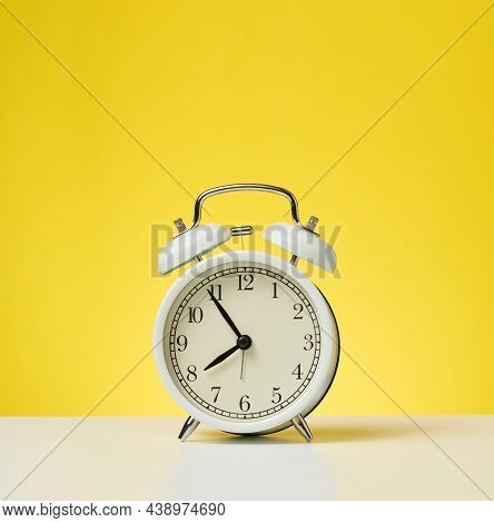 Round White Alarm Clock, Five Minutes To Eight In The Morning. Yellow Background