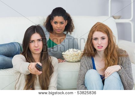 Portrait of serious young female friends with remote control and popcorn bowl on sofa at home