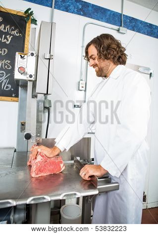Smiling male butcher slicing meat on bandsaw at store