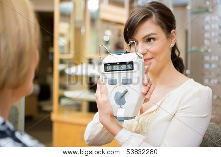Female optometrist showing pupilometer to mature woman in store