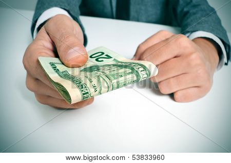a man wearing a suit sitting in a desk with a wad of american dollar bills in his hand