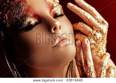 Art project: beautiful woman with golden make-up. Jewelry, make-up. Fashion. Over red background.
