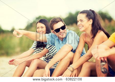 summer, holidays, vacation, happy people concept - group of friends pointing somewhere on the beach