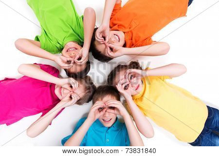 Five happy children lying on the floor in a circle with hands near eyes in bright t-shirts. Top view. Isolated on white.