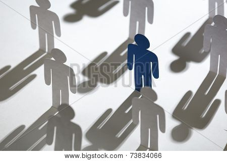 Close up of team of standing papermen. Lots of similar copies of a paper man, but a blue one stands out among them. Concept of teamwork and leadership