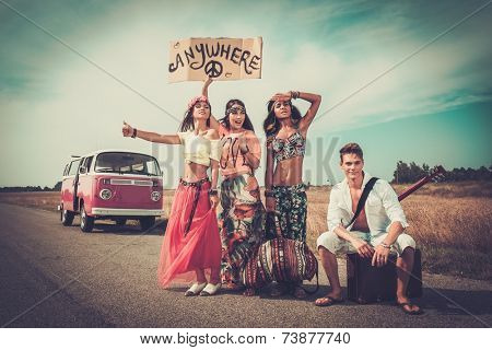 Multi-ethnic hippie hitchhikers with guitar and luggage on a road