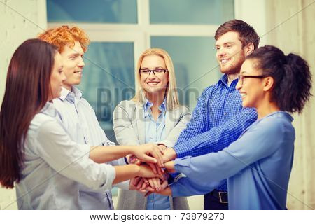 business, office, gesture and startup concept - smiling creative team with hands on top of each other sitting in office