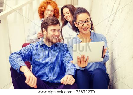 business, technology and startup concept - smiling creative team with tablet pc computer sitting on staircase
