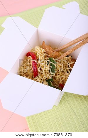 Chinese noodles and sticks in takeaway box on green napkin on pink background