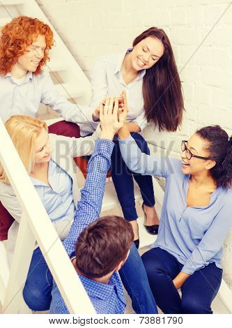 business, office, gesture and startup concept - smiling creative team doing high five gesture sitting on staircase