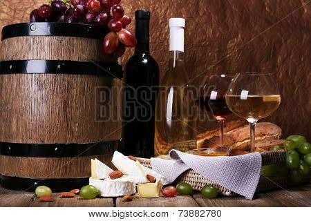 Supper consisting of Camembert and Brie cheese, wine and grapes on napkin in basket and wine barrel on wooden table on brown background