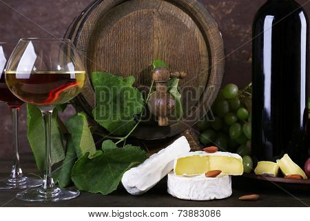 Wine in bottle and in goblet, Camembert cheese, grapes and wooden barrel on wooden table on wooden background