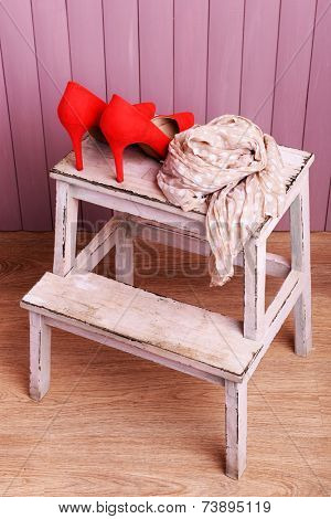 Red women shoes and scarf on bench on wooden background