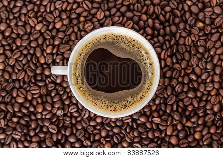 white cup of coffee on a heap of roasted coffee beans
