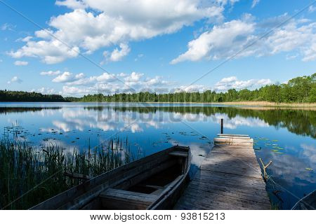 White Clouds On The Blue Sky Over Blue Lake With Boats And Boardwalk