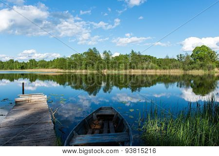 White Clouds On The Blue Sky Over Blue Lake With Boats And Boardwalk