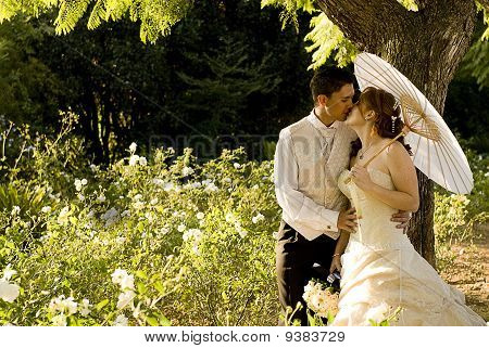 just married couple standing and kissing in white flower bed under a tree