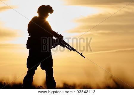 military. soldier silhouette in uniform with machine gun or assault rifle at summer evening sunset