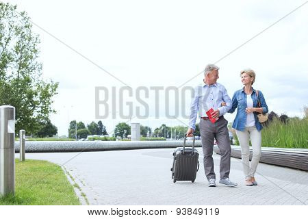Middle-aged couple with luggage walking on footpath against clear sky
