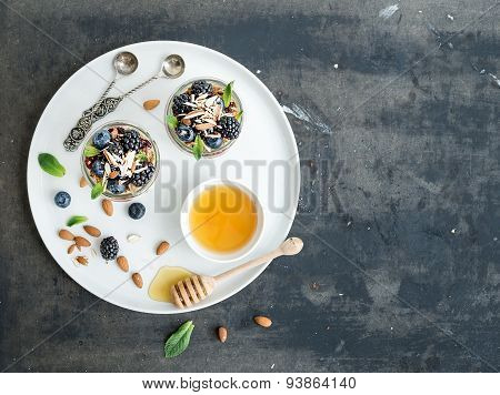 Yogurt oat granola with berries, honey and nuts in glass jars, dark grunge background