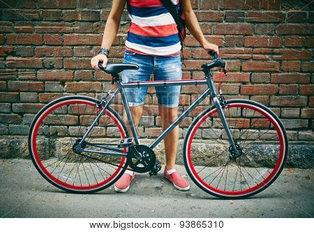Casual guy with bicycle standing by brick wall