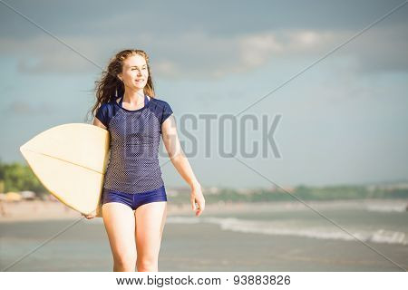 Beautiful sexy surfer girl on the beach at sunset walks along ocean shore, yellow surfboard in her h