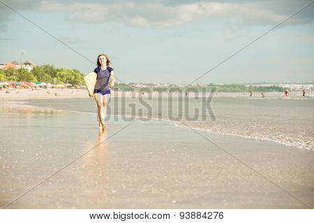 Beautiful sexy surfer girl on the beach at sunset walks along ocean shore, yellow surfboard in her h