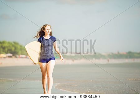 Beautiful sexy surfer girl on the beach at sunset walks along ocean shore, yellow surfboard in her h