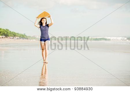 Beautiful sexy surfer girl on the beach at sunset walks along ocean shore, yellow surfboard in her h