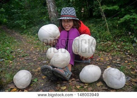 Girl with Giant puffballs sits on road in forest.