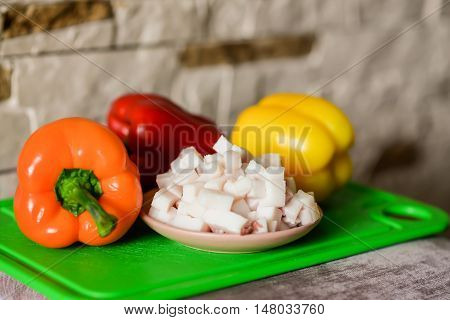 Lard cubes in small plate with colored bell peppers on green plastic board