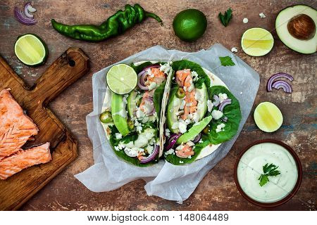 Preparing healthy lunch snacks. Fish tacos with grilled salmon red onion fresh salad leaves and avocado cilantro sauce on vintage stone background. Recipe for Cinco de Mayo party. Top view.