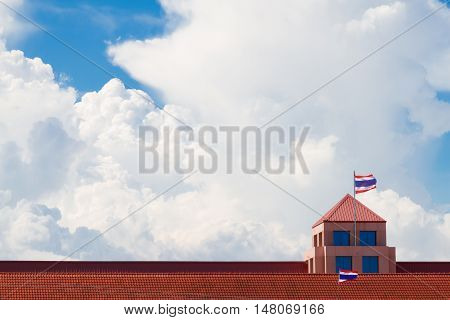 Red rooftop of school building against blue sky and white clouds .