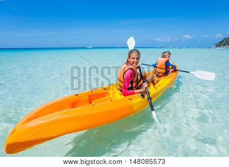 Kids enjoying paddling in orange kayak at tropical ocean water during summer vacation