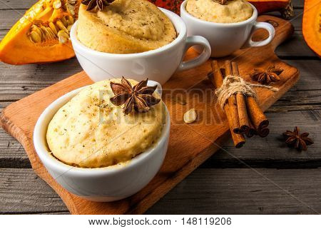 Pumpkin mug-cakes in rustic style, on an old wooden table, next to the cuted pumpkins and spices, close view