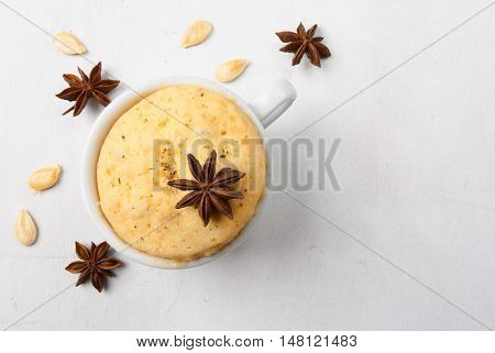 Pumpkin mug-cakes on a white wooden table, surrounded by spices and pumpkin seeds, top view, copy space