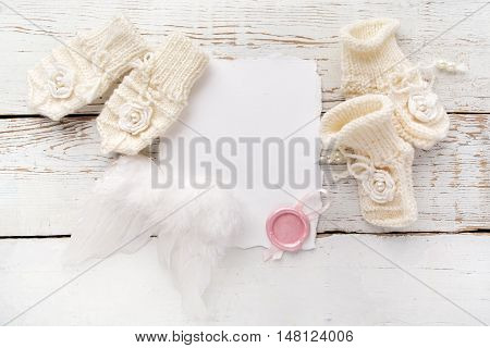 Baby New Born or baptism Greeting Card. Blank card with baby girl shoes, gloves and angel wings on white wooden background.