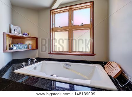 Close Up Of White Bathtub With Black Tile Trim And Wooden Shelf