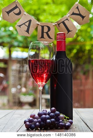 Bottle and glass of redd wine with party letters in park. Romantic lunch