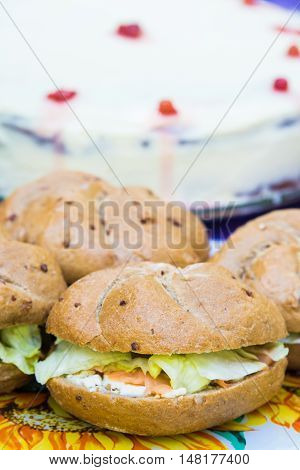 Close up of club salmon sandwiches arranged over a table at an open air garden party. Delicious cake in the background.