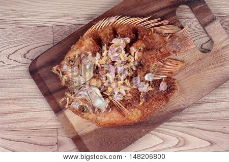 Deep fried fish ,Nile tiapia, with crispy garlic on butcher served. Top view
