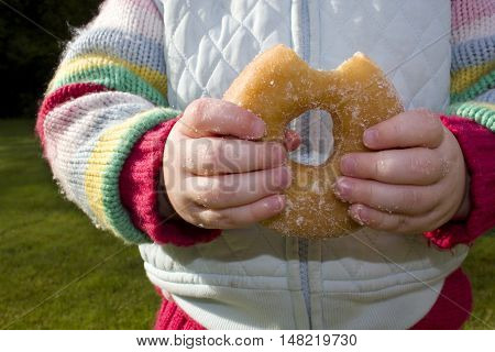 Young girl eating ring donut. Sticky fingers.